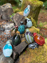 Load image into Gallery viewer, All eight sculpted dragon egg potion bottles displayed together at stone firepit ring on moss