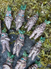 Load image into Gallery viewer, Hand sculpted mandrake rootling plant guardians with blue eyes and green sprout leaves, nestled in forest moss