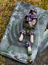 Load image into Gallery viewer, Sculpted polymer forest brooch with purple polka dotted mushrooms on a miniature stump environment, same style mushrooms dangling on bronze chain with added bronze bell. Made by The Woodland Wandolier, photographed on a mossy grey boulder

