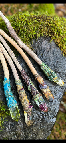 Handcrafted driftwood magic wands with resin crystals and floral designs, arranged on a mossy stone