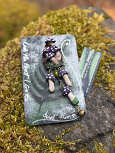Load image into Gallery viewer, Sculpted polymer forest brooch with purple polka dotted mushrooms on a miniature stump environment, same style mushrooms dangling on bronze chain with added bronze bell. Made by The Woodland Wandolier, photographed on a mossy grey boulder
