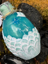 Load image into Gallery viewer, Pearly white dragon egg with pink and teal shadow washes, rounded overlapping scales, blue liquid settled, star charm
