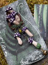 Load image into Gallery viewer, Sculpted polymer forest brooch with purple polka dotted mushrooms on a miniature stump environment, same style mushrooms dangling on bronze chain with added bronze bell. Made by The Woodland Wandolier, photographed on a mossy grey boulder
