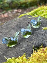 Load image into Gallery viewer, 3 clear resin lovebird figurines with moss and blue forgetmenot flowers inside them , ,in a row on a mossy stone
